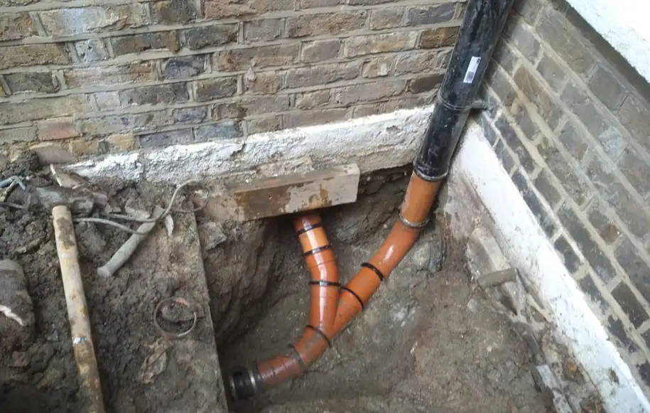 Excavation works to repair and replace damaged underground drainage pipework beside a building.