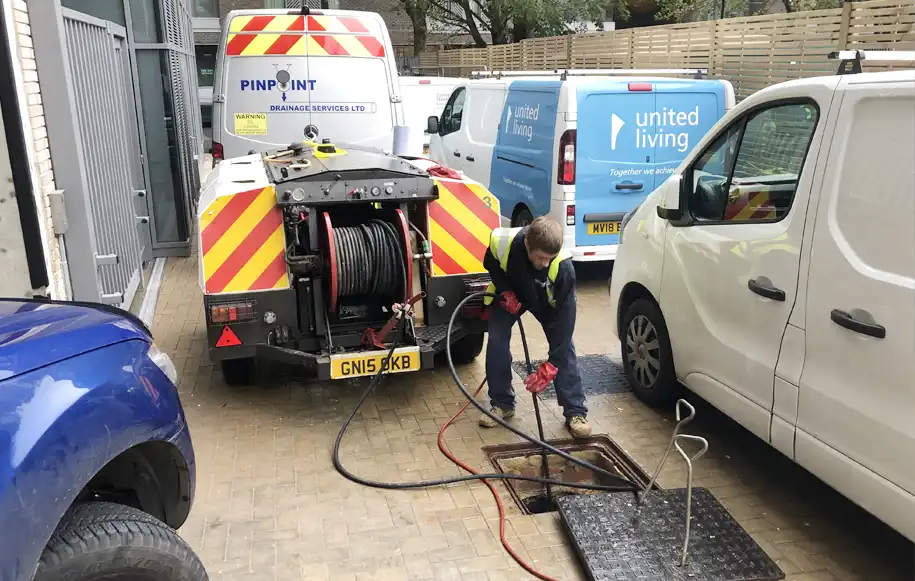Drainage engineer using high-pressure water jetting equipment to clean and unblock an underground drain.