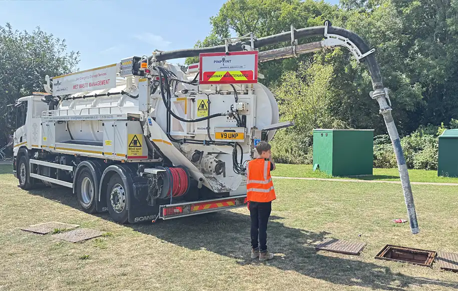 Vacuum tanker removing wet waste and sludge from an underground drainage chamber using a suction boom.