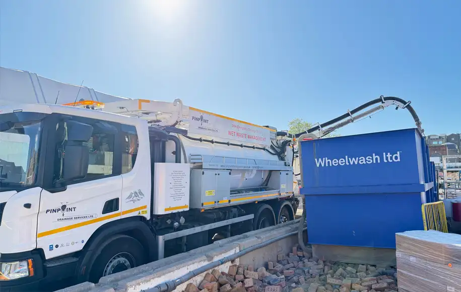 Vacuum tanker carrying out wash bay cleaning and waste removal at a construction site wheel wash facility.